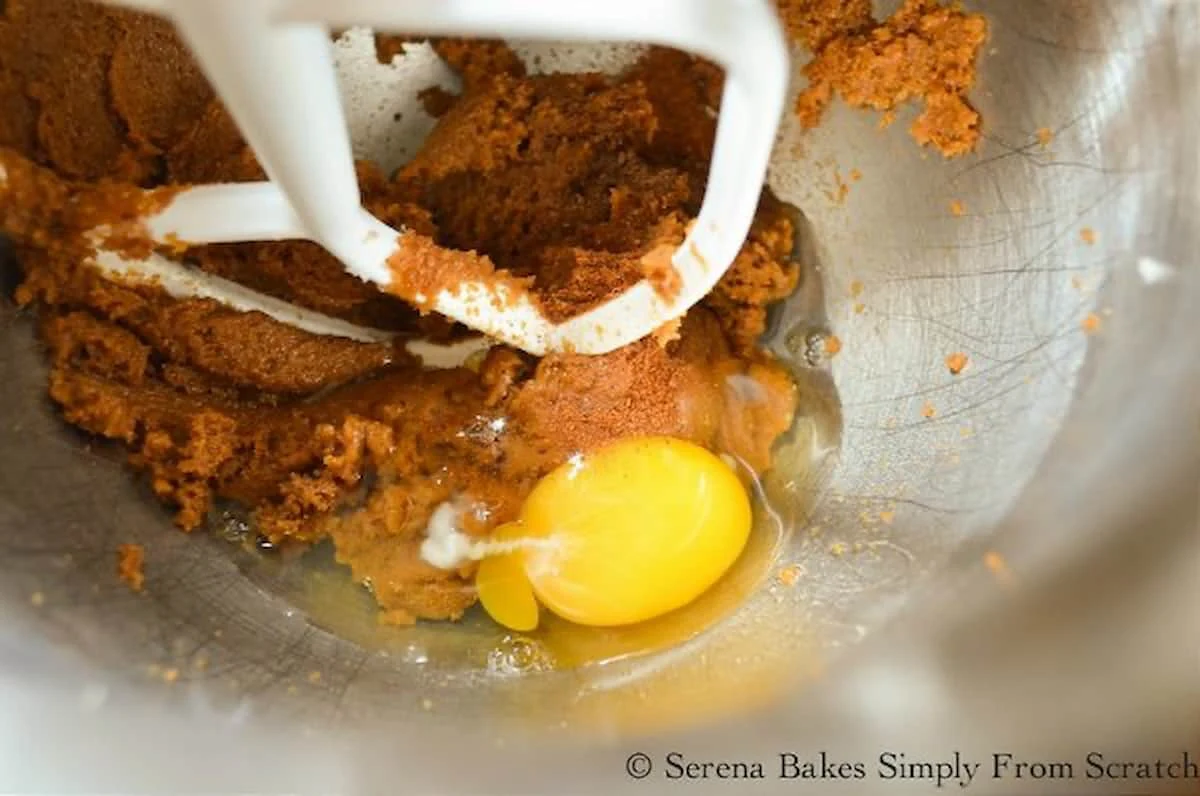 Egg added to Moist Pumpkin Bread batter in a stainless steel mixing bowl.