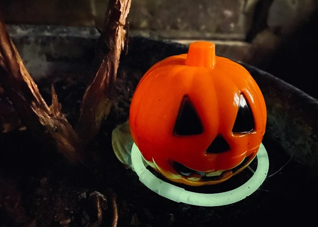 A plastic hollow pumpkin which opens to hide treats in, sitting in a flower pot and lit up by a glowstick