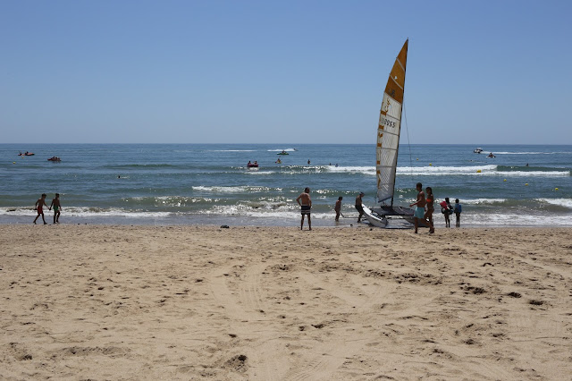 Playa llana de arena fina dorada con las azules aguas del océano al fondo y personas con una embarcación en la orilla.