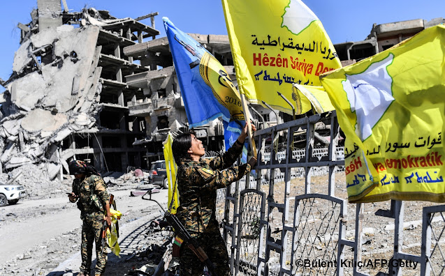 Żołnierze z Syryjskich Sił Demokratycznych (SDF) świętując zwycięstwo nad ISIS wieszając swoje flagi na rondzie  wśród ruin miasta