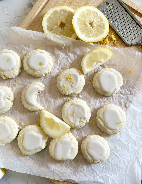 Lemon Meltaway cookies on parchment on a wooden cutting board, with sliced lemons.