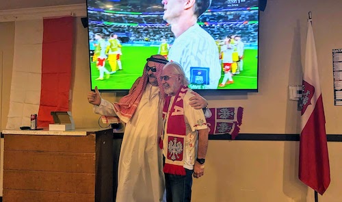 Two fans, one in Qatari cosplay, take a photo after the match