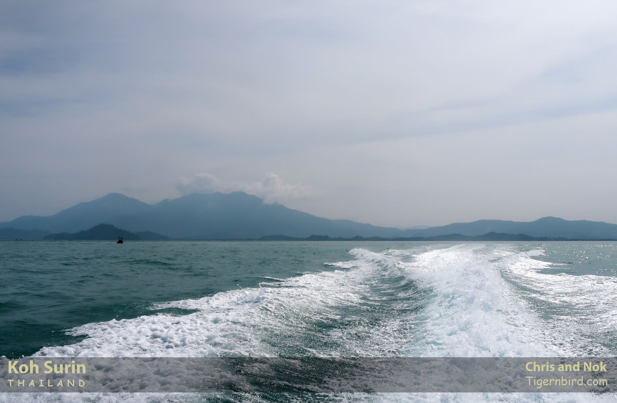 Speedboat wake in Andaman Sea on cloudy day with Thailand hills in background