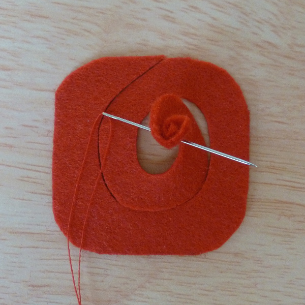 Sewing needle pushing through rolled felt fabric on a spiral