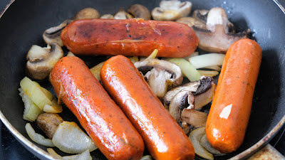 Vegan sausages browning in a frying pan with onion and mushroom.