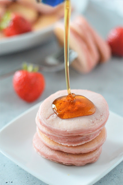 stack of mini pancakes on a white plate with syrup drizzling on top.