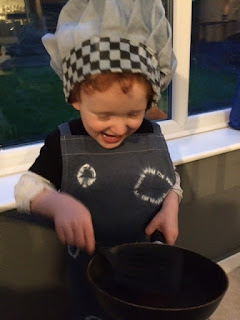 Very happy boy dressed as a chef holding a pan and spatula