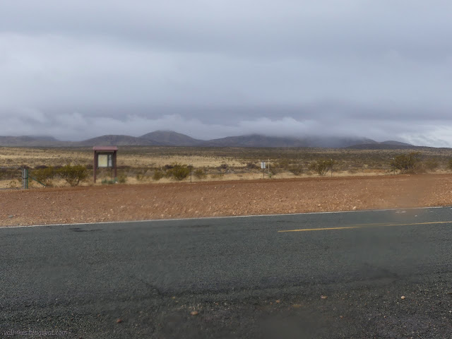 00: flat road, flat desert, clouds settling down on low mountains in the distance