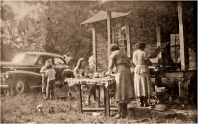 Old picture of family dining in front of a house.
