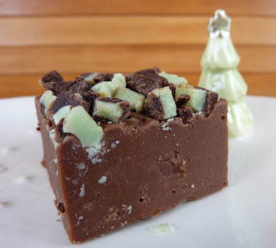 I piece of Chocolate Irish Cream Fudge, topped with Andes mint chips. Photographed on a white plate with a small Christmas tree.