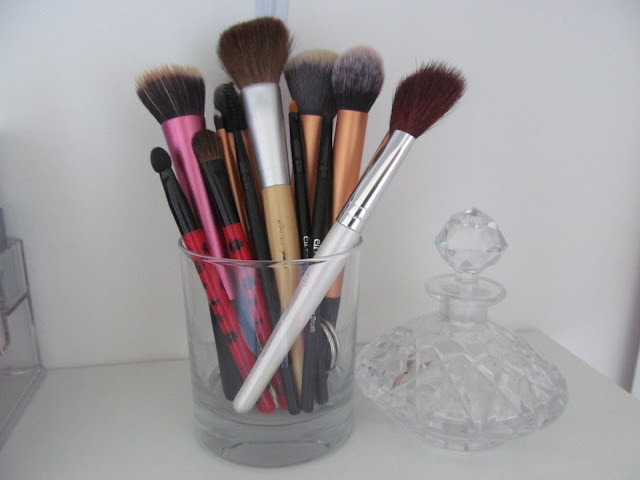 makeup brushes small and large in glass jar next to small crystal glass decanter