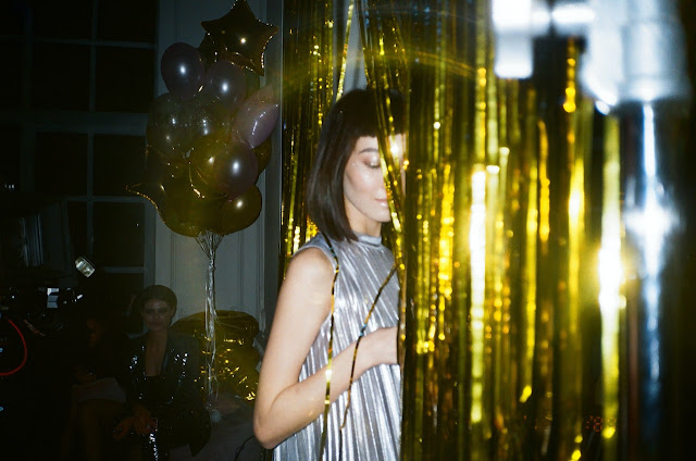 Yourng woman in silver party dress going through a curtain wo gold glitter ribbons.