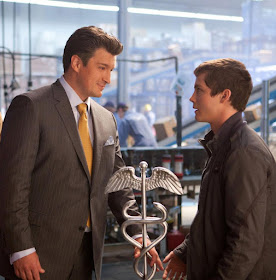 Nathan Fillion (Hermes) y Logan Lerman (Percy) en en una imagen oficial de la película El Mar de los Monstruos. Están hablando y entre ellos está el caduceo del dios (con las serpientes Martha y George).