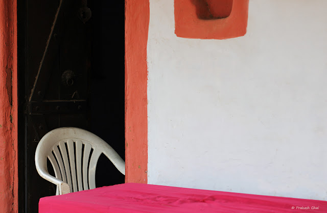 A partially visible White Chair placed in front of an open brown door at The Village area at Jawahar Kala Kendra, Jaipur, India.