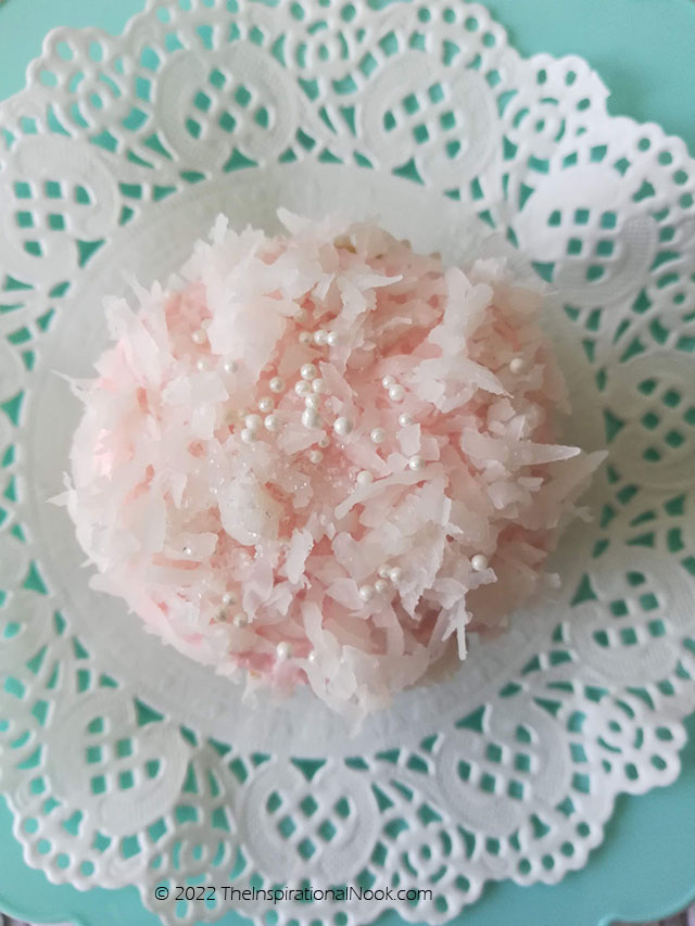 Coconut cupcake, Pink frosted cupcake topped with dessicated coconut and sugar pearly on a lace doily