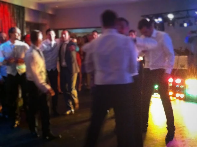 A blurred photo of a group of men dancing at a wedding with disco lights in the background