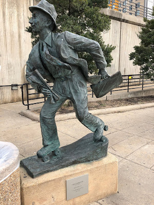 Photo of The Commuter statue. There is part of a garbage can in the photo right in front of him.