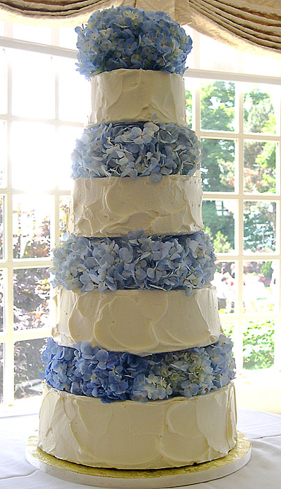 Four tier round white frosted wedding cake with bunches of blue hydrangeas