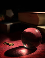 Close up photo of a dimly lit crystal ball laying on a table in front of a stack of large books and with a key laying next to it