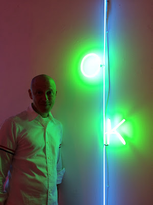 iPhone 5s photo by Jenny Lam of Jason Pickleman next to his neon piece in his 2019 art exhibition "Light Reading" at Ken Saunders Gallery in Chicago