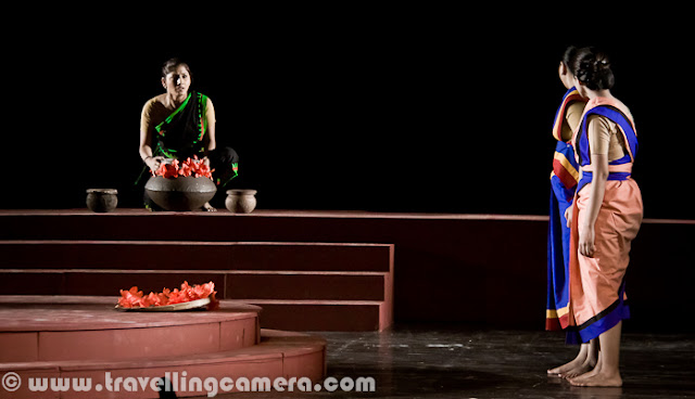 Here are some more pictures from the play Chandalika. To give you some context of the play, it was written by the legendary Rabindranath Tagore and it is the tale of Prakriti, an untouchable girl forced to live on the periphery of society as ‘chandalika’. No one want to play with her, people keep distance from her but at times interact with her for their personal benefits. The play is based on a story from a Buddhist text. Play starts with some dialogs by Usha Ganguli where she describes the situation of her region without water and how people are crying for water. Usha is playing main role in this play. She has a daughter and both of them are treated badly by higher society. At the same time, she helps the local kingdom by helping in various problems like water scarcity. Setting and expressions are two powerful tools used to assist dialogs and action in drama for conveying important information to the viewers. Through these tools a lot can be shown without actually being said. For example, firewood, earthen pots etc. show a rural setting and may also indicate that the play is set in past. Everything cannot be expressed in words because then  the play will be much too lengthy, boring and unintelligent.Interactions between characters, their expressions and their actions often hide a subtext that is very interesting to unearth. For example, in this scene, can you make out what the character is feeling of thinking without actually knowing what is going on? One can easily assume that the character is not unhappy and may even be pleased about things. I can also see a hint of dreaminess in the eyes and may be lost in thoughts about her beloved. But then that is my interpretation and how close it is to the actual emotions being portrayed by the character depends upon the character's acting skills and my ability to read expressions. The expressions here are more of defiance and questioning. But then again that is my interpretation and I can be wrong. Another thing you'd want to note is the attire and the make-up. All efforts are made to keep them true to the situation, the period, and the story. For example, here the dhotis and the lathis indicate that the setting is rural and the expressions of various characters indicate their emotions. For example, the person who is chained is reluctant to go where he is being led and the person in the red dhoti seems to be pleased with himself and takes pleasure in the predicament the chained person is in. Flowers, dances, audience, claps indicate celebrations of either a festival or an event. Some people are wearing garlands and this may indicate their special place in the society. Graceful dance moves and melodious singing are all often a part of dramas and I am amazed by the number of talents most of the stage artists hide within themselves. Almost all of them sing well and dance well along with obviously acting well. One-on-one interactions are some of the most interesting interactions in a play. They reveal more about a character and her relationships with other characters than any other interaction in a play. These are usually more difficult to carry out because the audience is focussed upon the characters involved. These are more challenging for the actors than for the directors.Multiple characters interactions are more challenging for the playwriter and for the director because it requires exceptional skills to craft such scenes. Colors and body languages tell stories of themselves. The next time you go to watch a play, try to keep an eye on these things and you will be amazed at what you will discover.Presence of objects such as cages can be symbolism that you had never suspected. If you observe these things, you will add layers to your play-watching experience. For example, here it is clear that the woman in the centre is someone who has power over the other two. The cage represents imprisonment or curtailment of freedom. The attire of this woman indicates affluence and her demeaner indicates power and even royalty. Is there anything else you can make out? Feel free to leave a comment if you can. The body language of the characters here indicates a mother-daughter relationship. And the leaves and the leaves indicate some sort of a ritual or religious practice. The clothes of these two characters are much simpler. The characters are not affluent but aren't poor either. Let me know if you can read more into these pictures. I would love to know. Please feel free to leave a comment.