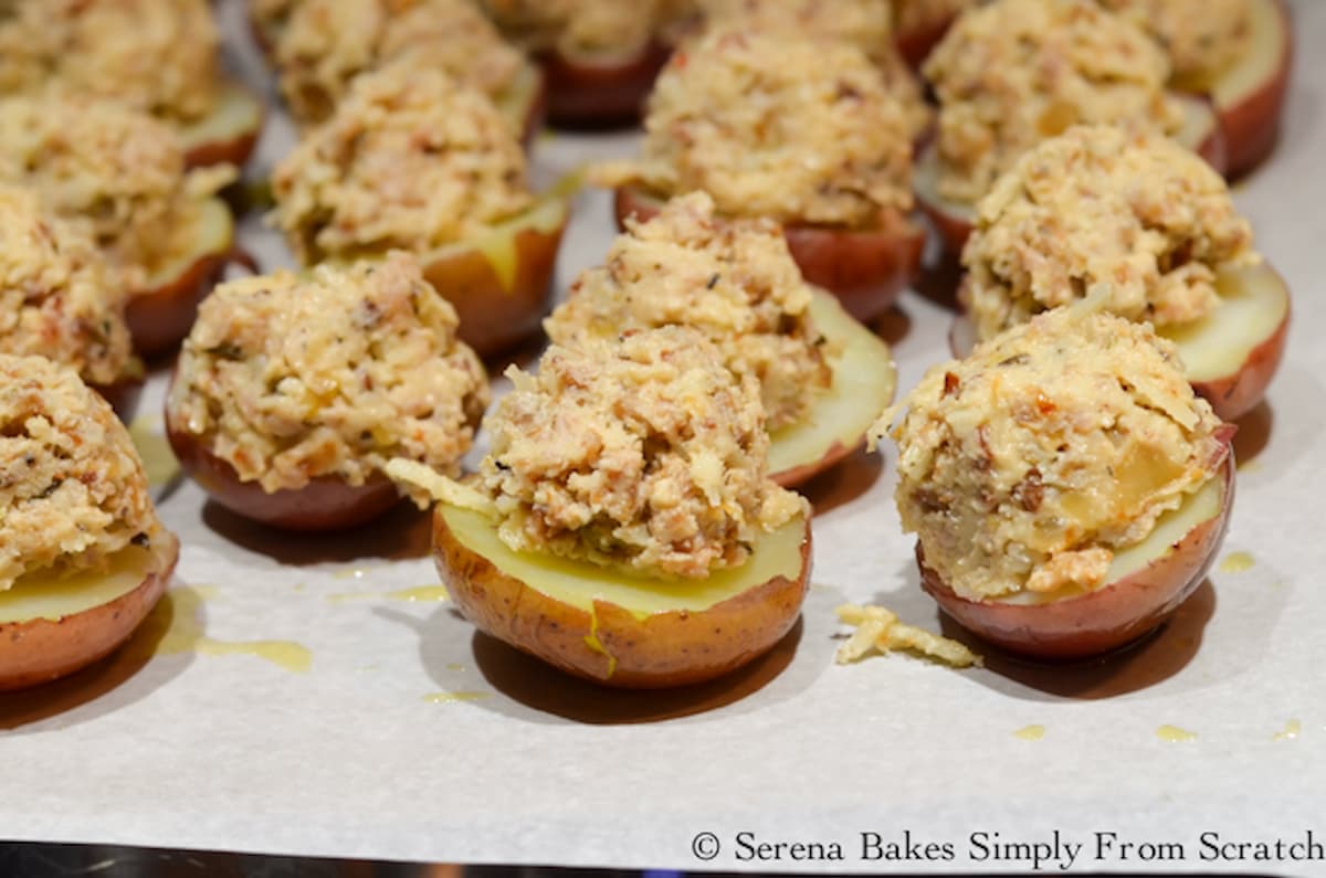 Half mini red potatoes on a cookie sheet lined with parchment paper and topped with cheesy sausage mixture.