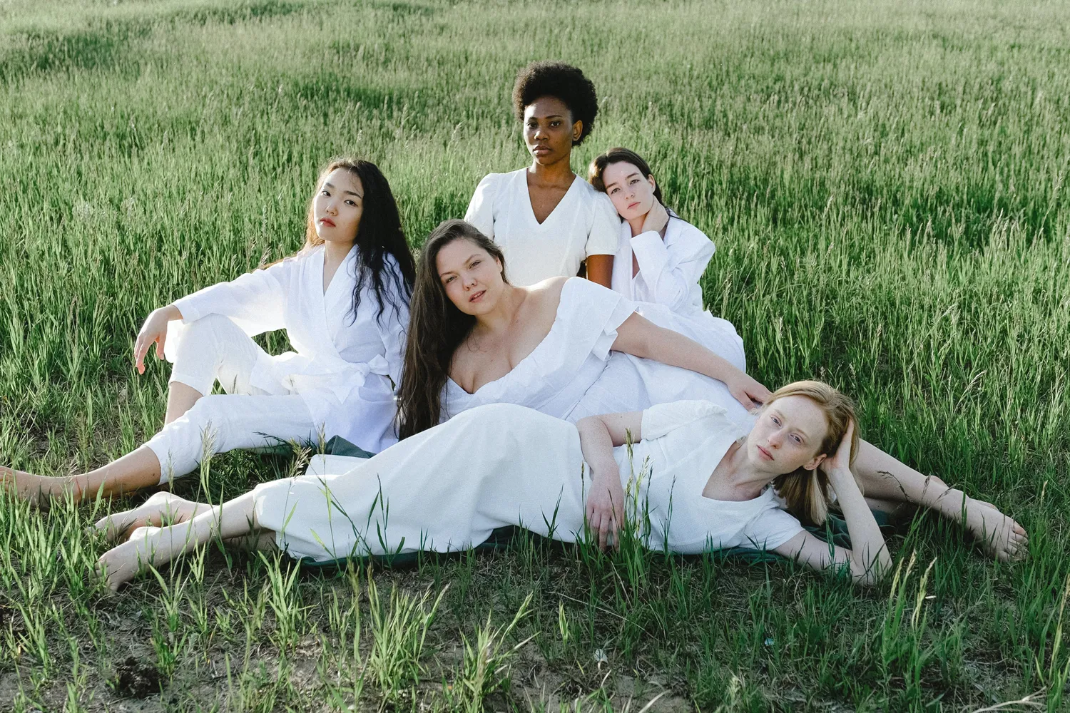 a group of women in light clothes, they lay on the grass