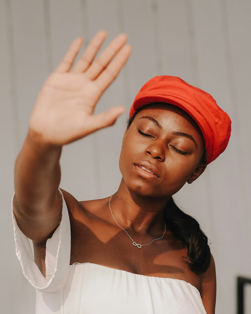 dark skinned woman wearing red cap and white top eyes shut holding hand up to camera:Photo by natasha tirtabrata on Unsplash