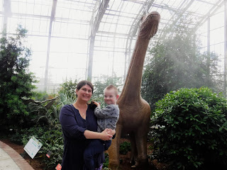 a mom and son smile together in front of an apatosaurus statue and tropical plants at Lauritzen Gardens