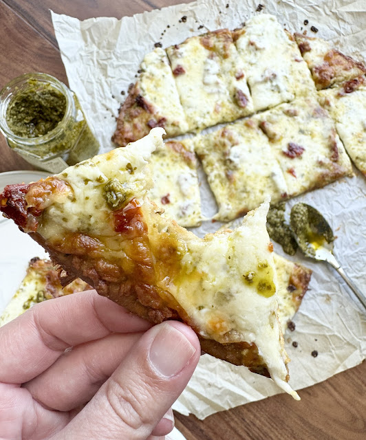 A hand holding a slice of sun dried tomato & pesto pizza.