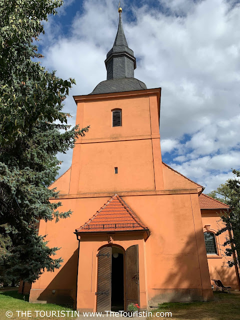 Small terracotta-orange painted village church with the brown wooden door open..