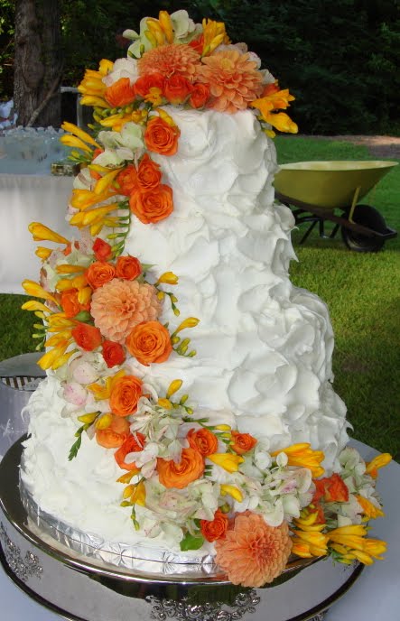 Three tier round white wedding cake with bright orange roses and silver lace