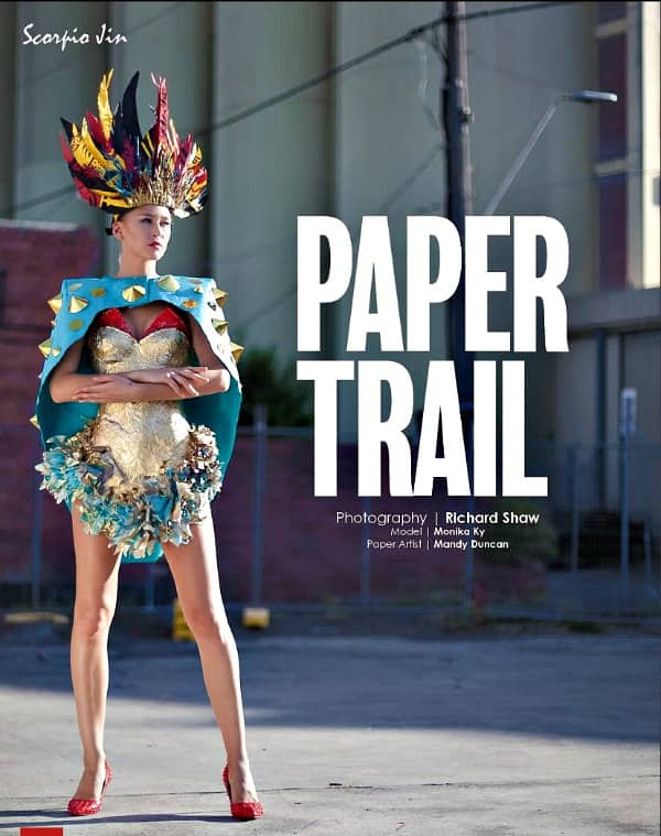Scorpio Jin magazine cover image of young female model standing and dressed in short, vivid paper outfit with cape and elaborate paper feather headpiece