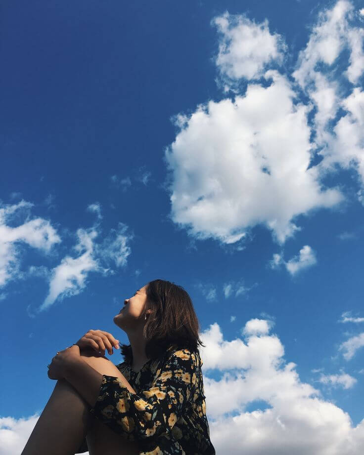 Foto tumblr chica sentada con nubes de fondo