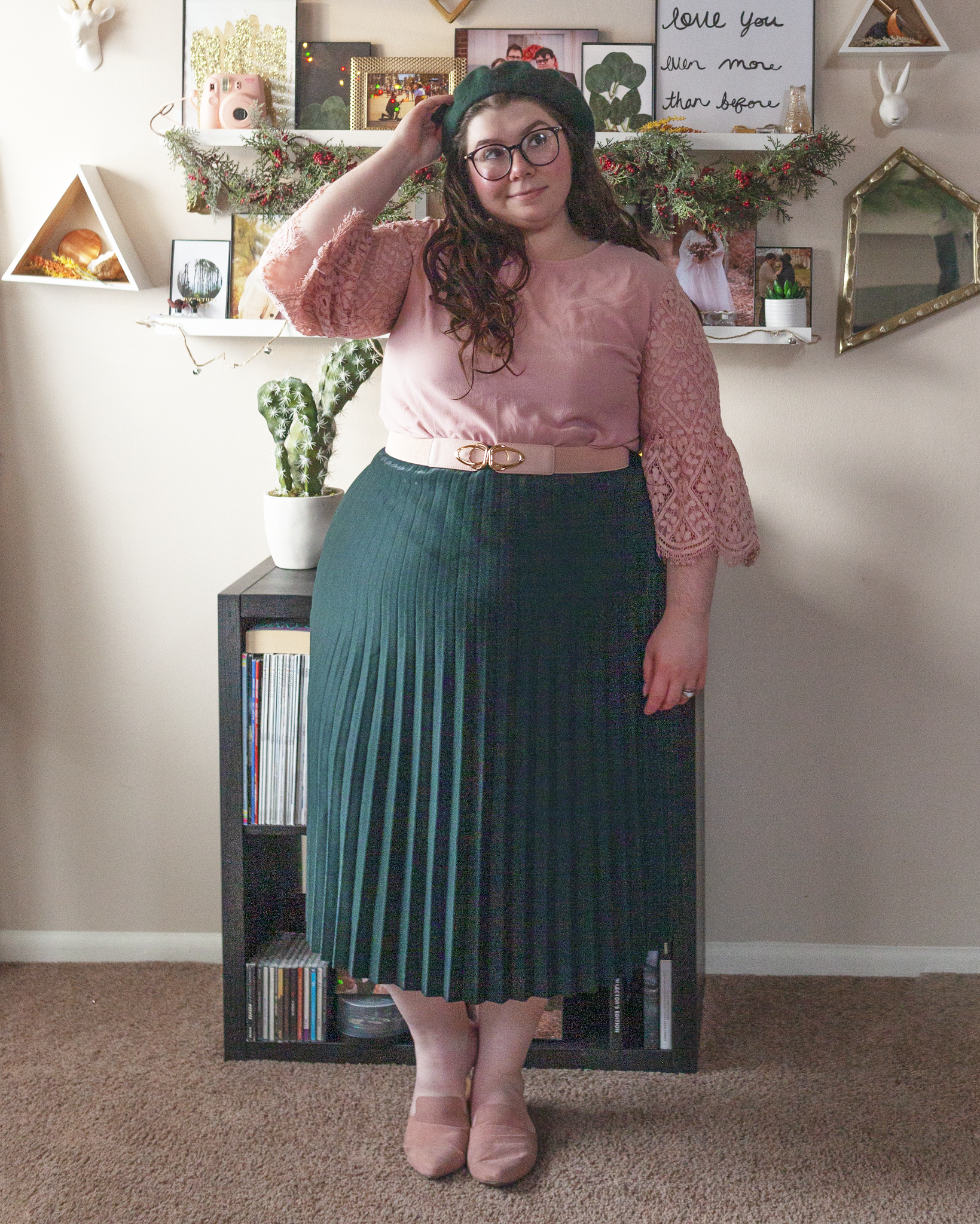 An outfit consisting of a pastel pink dress with lace flounce sleeves, tucked into a green pleated midi skirt and pink mules.