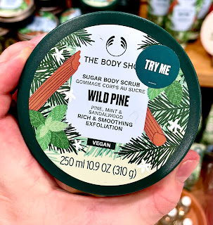 A close up of a circular silver metal pot filled with white cream with a silver circular lid with a white label with wild pine body butter the body shop in black font on a bright background