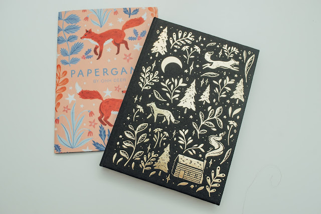 A black hardback notebook with gold foiled floral, leaf and fox illustration