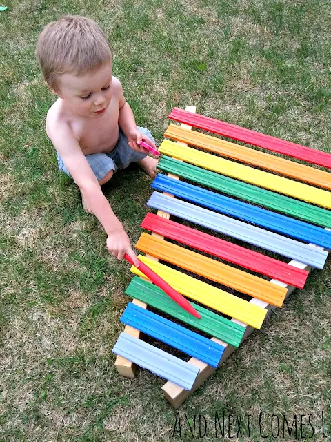 Kid playing on a homemade rainbow xylophone in the backyard