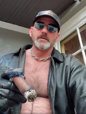 1/12 handsome man in late forties with a beard salt and pepper wearing leather hat, jacket that is shirtless open and hat while smoking a cigarette squirting a flashy silver chain around there
