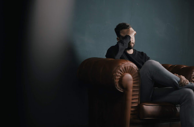 Bearded man sitting on a leather couch with his head leaning against one of his hands