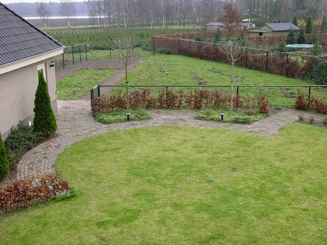 Tuin met saai grasveld en twee sprietige boompjes