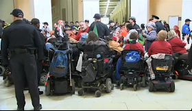 Protesters in wheelchairs viewed from behind, indoors