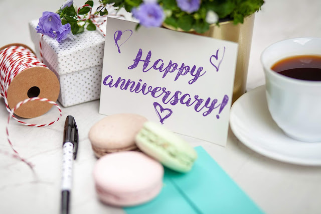 A table card with a "Happy Anniversary!" text, and surrounded by coffee, twine, gift box, and macarons.