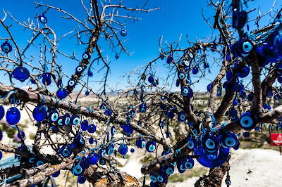 A close-up of bare tree branches with light & dark blue colored circular evil eye amulets. Photo by Hulki Okan Tabak.