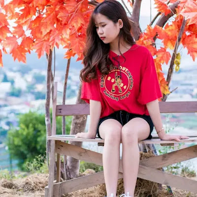 An image of a very cute beautiful girl wearing a red top sitting on the table under the golden leaves tree- sad girl dp