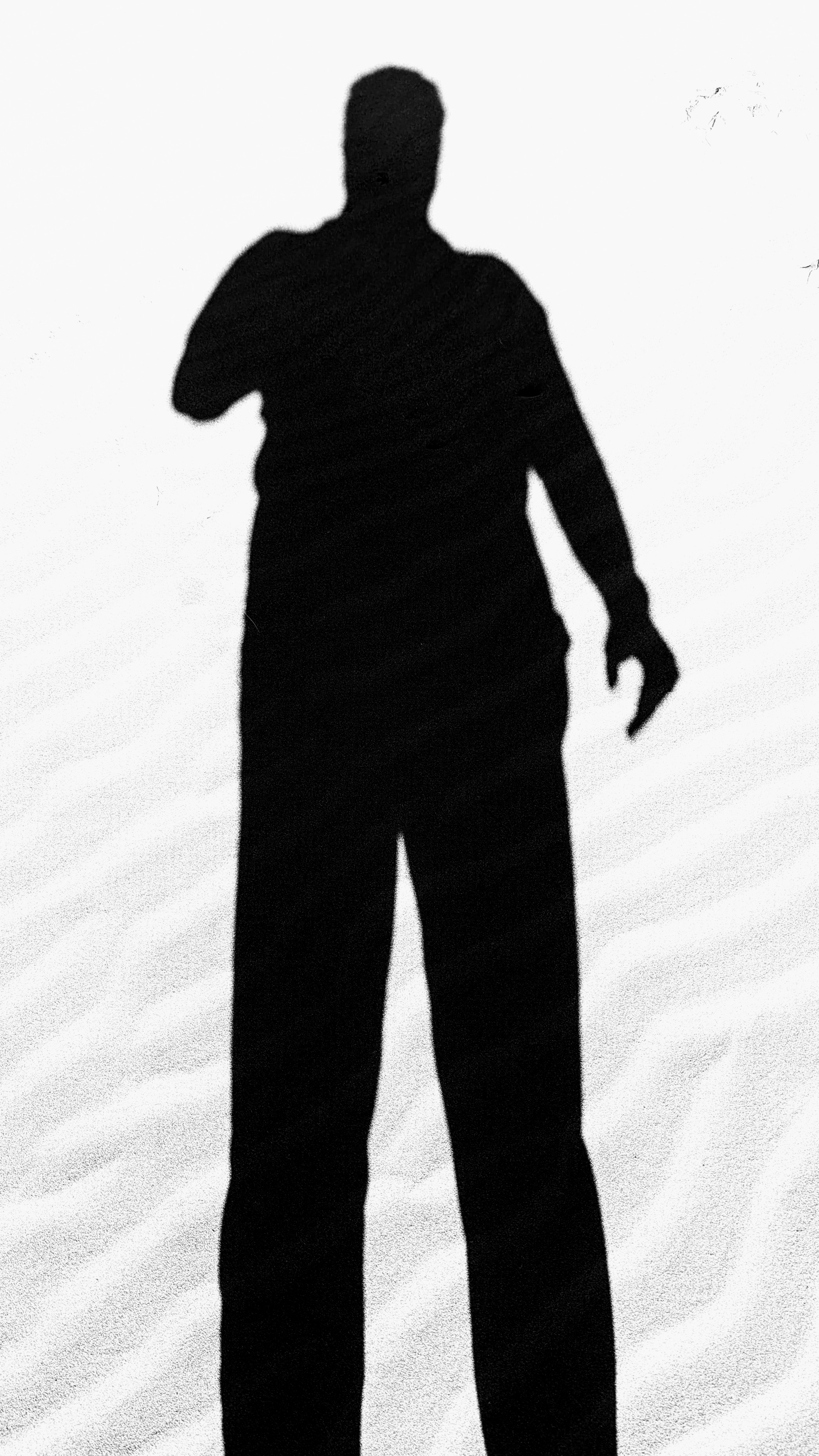 Edited and with stark contrast this photo shows a selfie shadow of a man on a rippled beach.