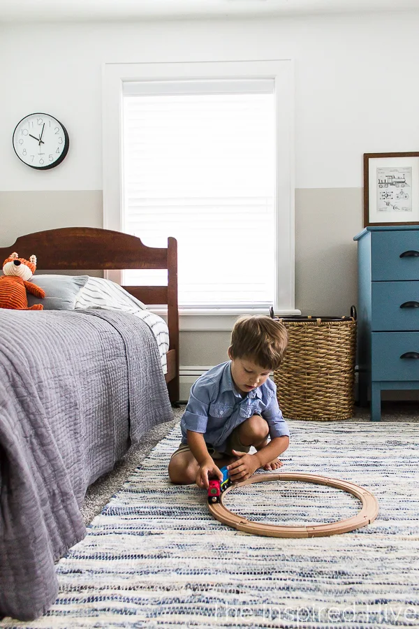 Playing with toy trains in boy's bedroom. Denim rug and antique bed. 