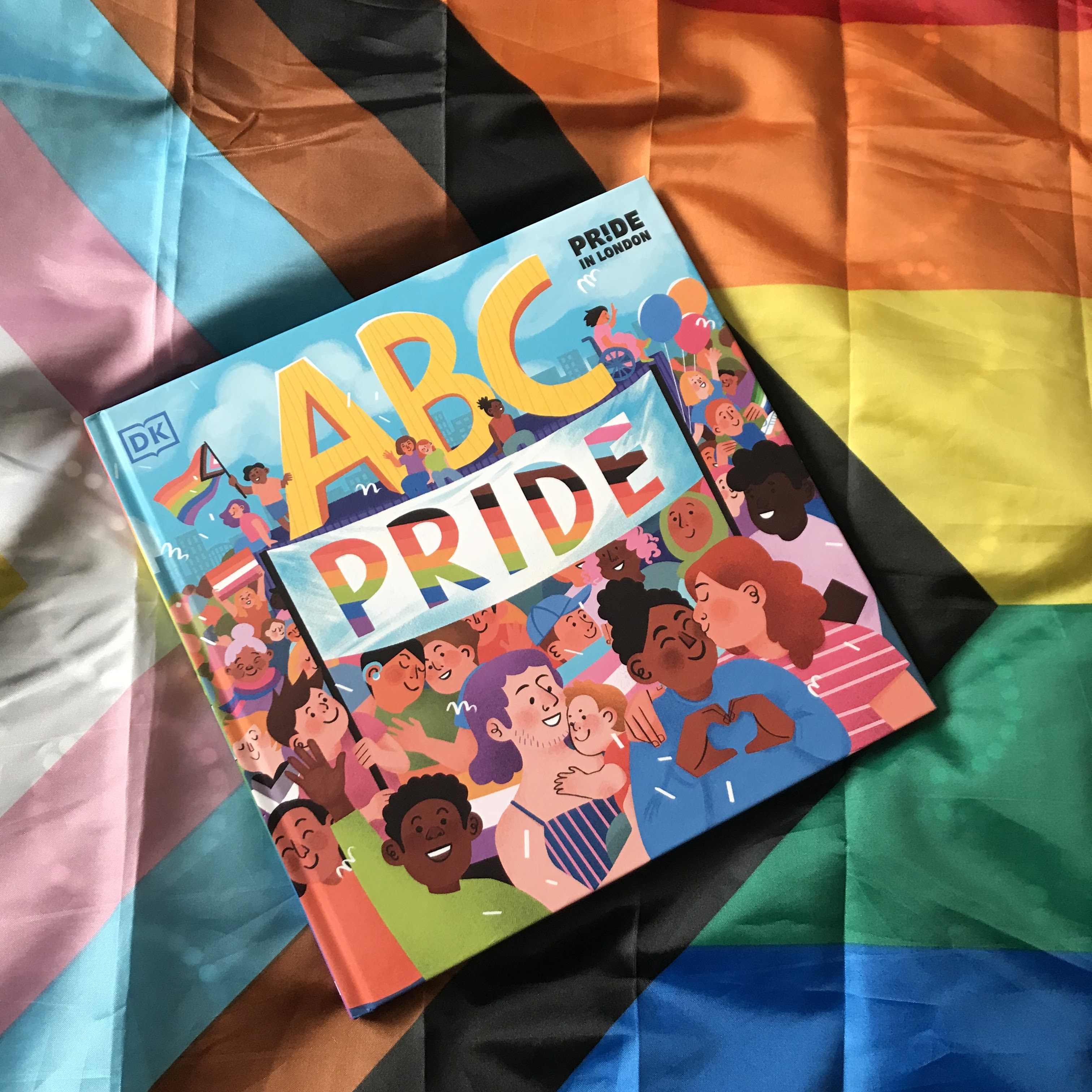 ABC Pride by Dr Elly Barnes MBE, Louie Stowell and Amy Phelps on a Progress Pride flag at a diagonal, top left to bottom right.