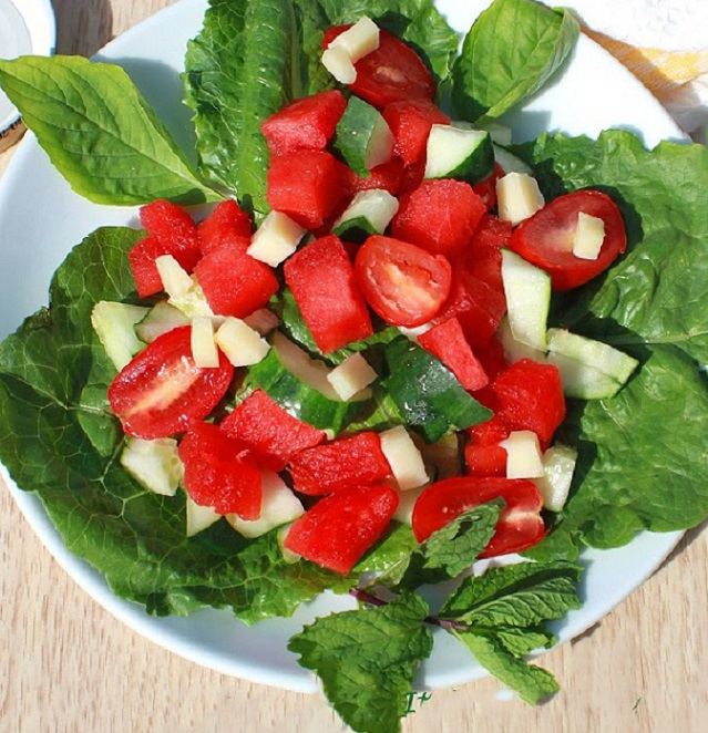 a fresh salad made with watermelon, cheese tomatoes and lettuce with basil