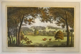 A landscape featuring sporadically wooded hills and a cluster of cows.